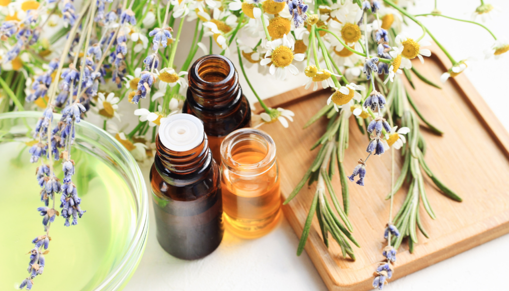 Frascos de óleos essenciais ao lado de flores de lavanda, camomila e alecrim em uma tábua de madeira, representando aromaterapia e bem-estar natural.