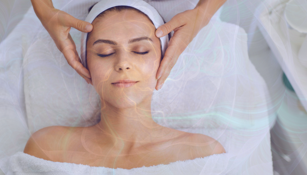 Mulher sorridente relaxando durante uma massagem facial, com suaves efeitos de luz fluindo ao redor, simbolizando equilíbrio e serenidade.