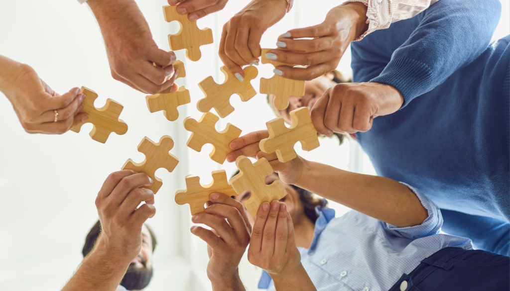 Grupo de pessoas segurando peças de quebra-cabeça, representando trabalho em equipe, colaboração e a construção conjunta de soluções.