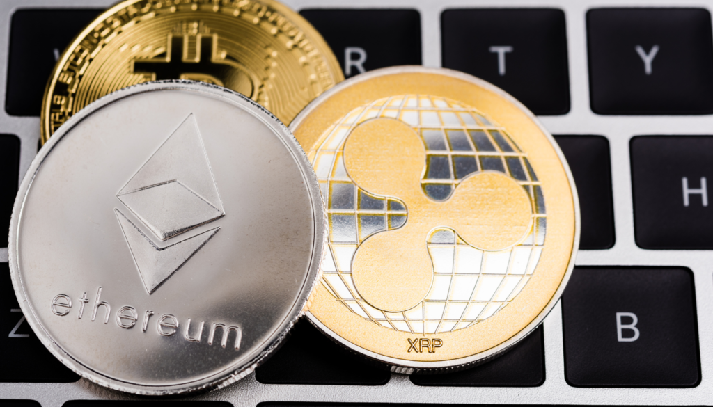 Como usar criptomoedas no mundo digital. Moedas físicas representando Ethereum, Bitcoin e Ripple (XRP) posicionadas sobre um teclado de computador, simbolizando o uso de criptomoedas no ambiente digital.