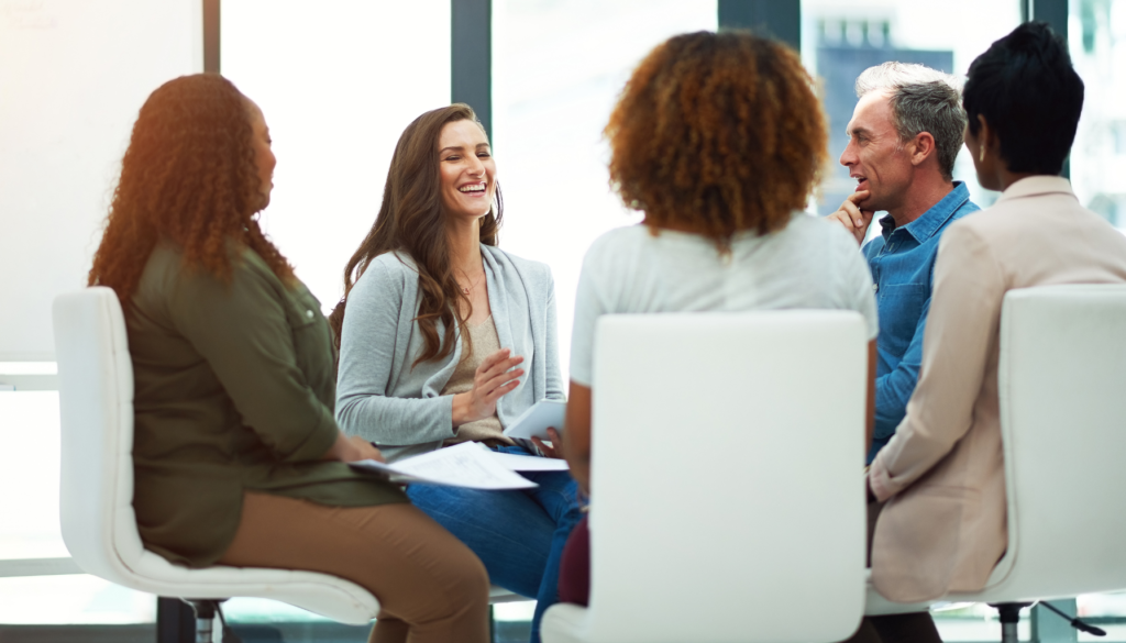 Grupo de pessoas sentadas em círculo em um ambiente de trabalho, participando de uma conversa colaborativa e descontraída.