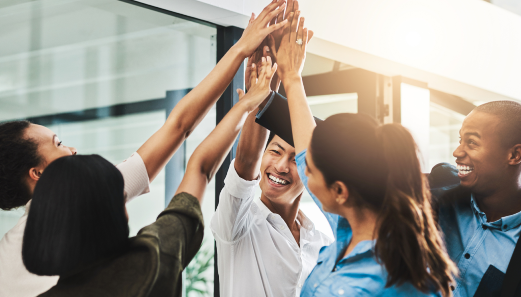 Equipe diversa comemorando com um toque de mãos em grupo, simbolizando união e celebração de conquistas no ambiente de trabalho.