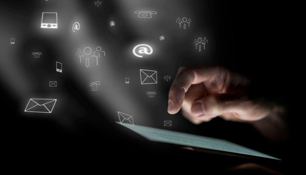 Pessoa interagindo com ícones digitais de comunicação, como e-mail, telefone e contatos, representados em luz flutuante sobre um fundo escuro.